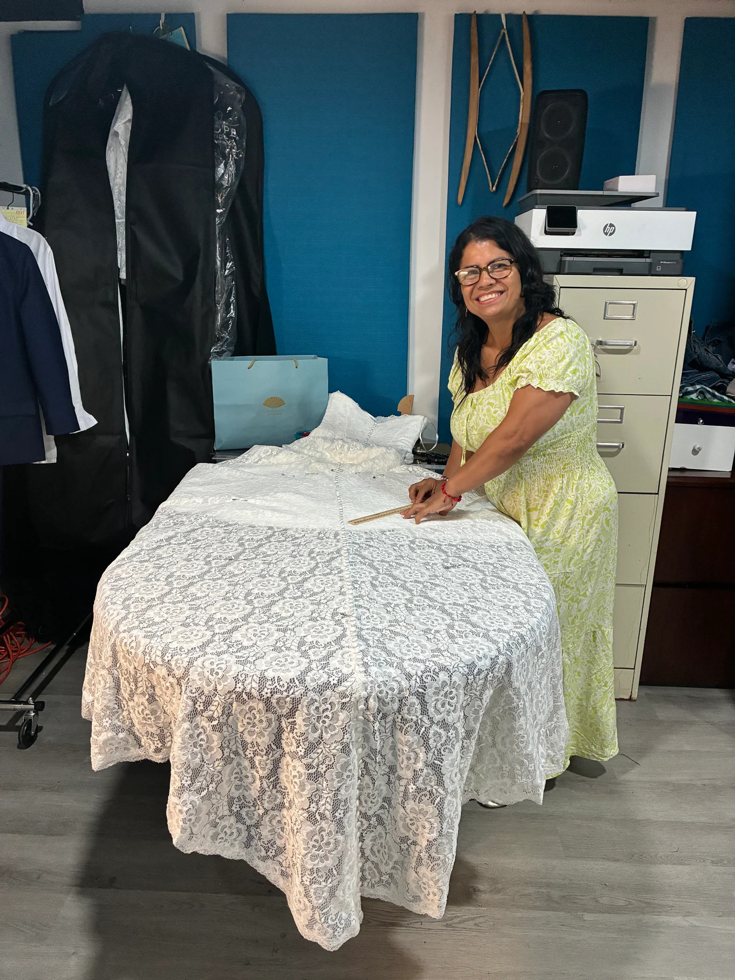 Esperanza smiling as she measures a lace bridal gown at her work table